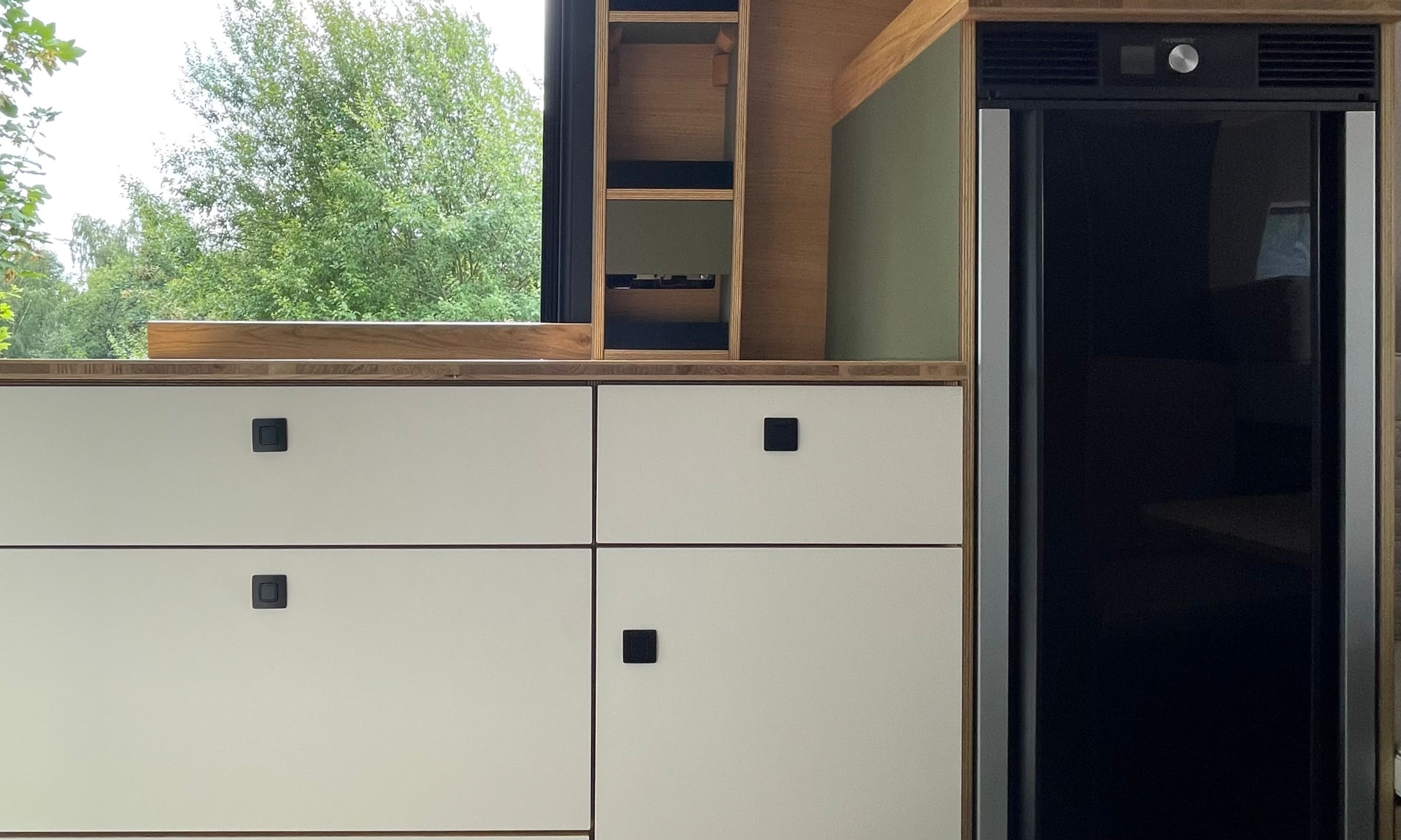 Küchenzeile mit weißen Fronten, Holzarbeitsplatte und Kühlschrank im domosMobil